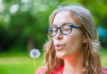 Verano: plantas medicinales y silvestres en el campo y el bosque A young woman holds an dandelion in her hand and blows