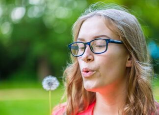 Verano: plantas medicinales y silvestres en el campo y el bosque A young woman holds an dandelion in her hand and blows