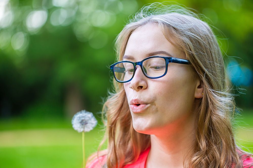 A young woman holds an dandelion in her hand and blows