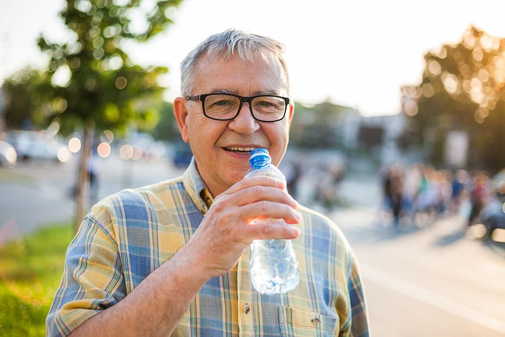 Happy senior man is drinking water in the city.